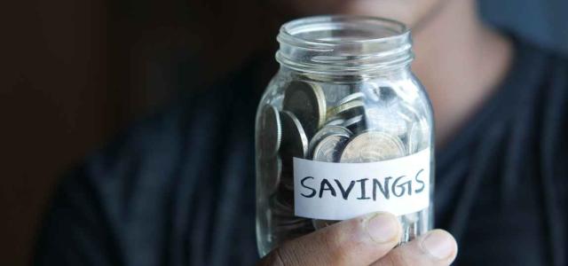 Person holding jar of coins with a 'savings' label